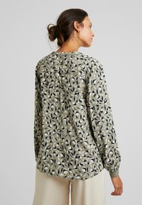 Blusa verde com padrão de folhas em azul-marinho e creme. Mangas longas, decote redondo e um corte ligeiramente solto. Textura suave.