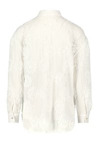 Blouse blanche avec broderie florale, manches longues, poignets à boutons et col classique. Tissu semi-transparent avec des détails en appliqué texturé.