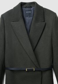 Dark green wool blend coat with notched lapels, structured shape, and a slim black belt with metallic accents at the waist.