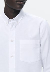Camisa blanca de botones con cuello, pequeño bolsillo en el pecho y sutil bordado de la "W". Fabricada en una tela de algodón texturizada con detalles de botones.