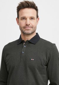 Mørkegrønn langermet polo skjorte med en marinebl�å krage, tre knapper og en liten rød, hvit og blå logo på brystet. Matt tekstur.