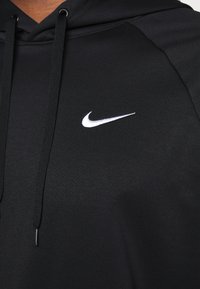 Gros plan sur un sweat à capuche noir avec des cordons noirs et un petit logo Nike swoosh blanc sur la poitrine.
