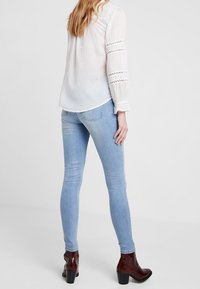 Ljusblå skinny jeans med en mjuk textur, hög midja och en lätt blekning. Bärs med mörkbruna klackstövlar med en glänsande yta.