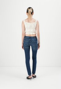 Vitt kort topp med volanger och elastisk kant, i kombination med figurnära blå denimjeans med bakfickor och en lätt blektoning.