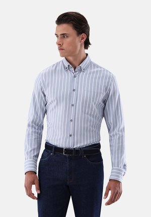 Himmelblaufarbenes langärmliges Hemd mit weißen vertikalen Streifen, Button-Down-Kragen, einer Brusttasche und Knöpfen entlang der Vorderseite. Kombiniert mit dunklen Jeans.
