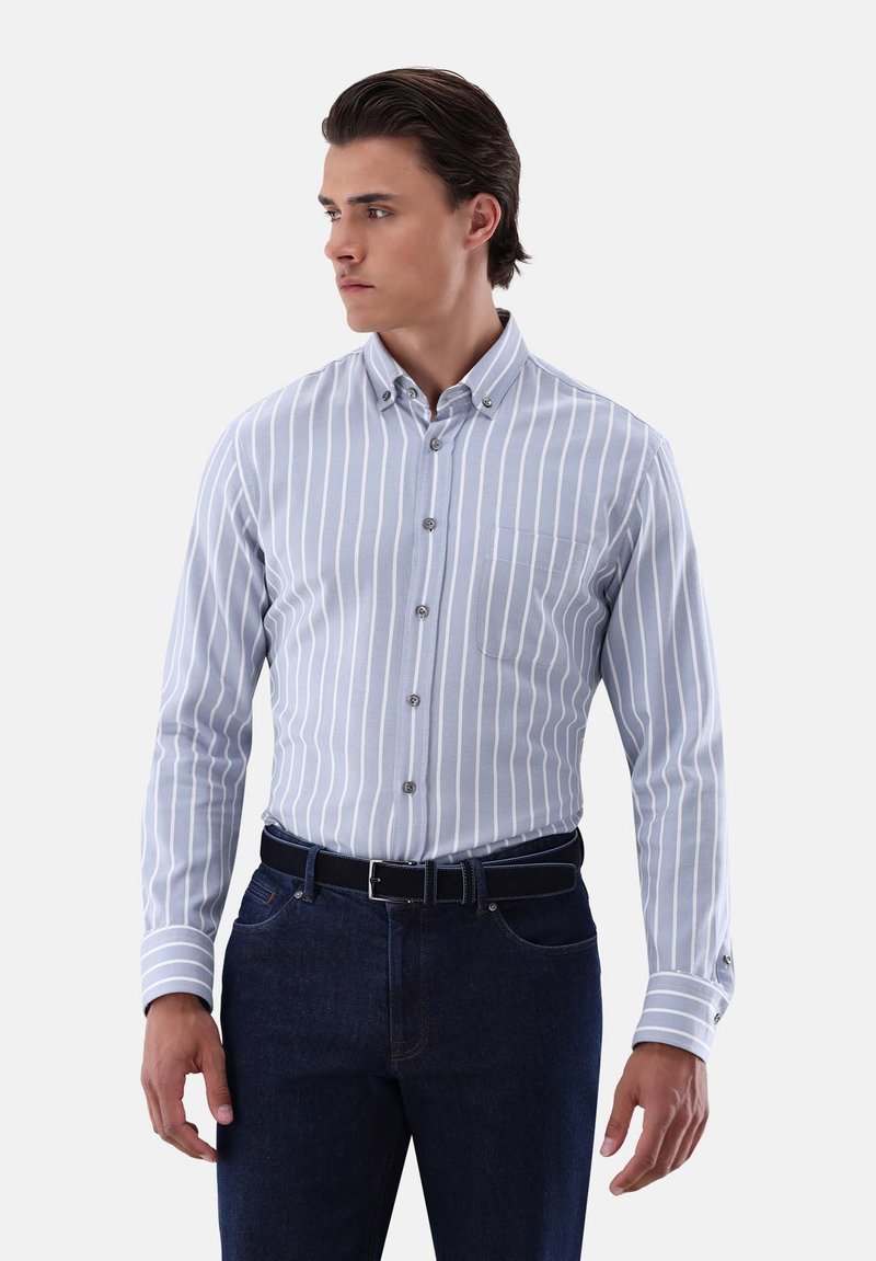 Himmelblaufarbenes langärmliges Hemd mit weißen vertikalen Streifen, Button-Down-Kragen, einer Brusttasche und Knöpfen entlang der Vorderseite. Kombiniert mit dunklen Jeans.