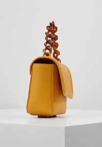 Sac à main en simili cuir jaune, de forme structurée, avec un fermoir à rabat sur le côté et une anse décorative en chaîne marron. Texture lisse, design minimaliste.