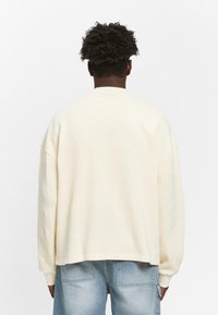 Crème-kleurige, textuurgebreide sweatshirt met verlaagde schouders en een korte achterkant, gecombineerd met lichtblauwe, licht vervaagde spijkerbroek.