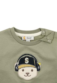 T-shirt in cotone verde con scollo rotondo, caratterizzato da un design ricamato di testa d'orso con cuffie e un cappellino nero e giallo.