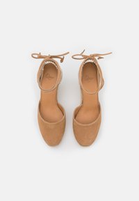 Scarpe con tacco alto in suede color sabbia con lacci alla caviglia, senza retro e suola piattaforma in juta naturale. Fodera interna liscia con logo del marchio.