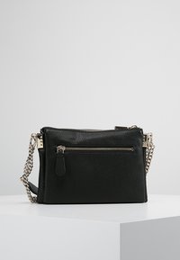 Czarna skórzana torba na ramię z teksturowaną powierzchnią, z zamykanymi kieszeniami i srebrnym łańcuszkiem jako paskiem. Zawiera mały detal w postaci metki.