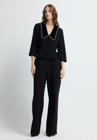 Černý dokonale střižený komplet s sametovým límcem, zapínáním na knoflíky, peplum pasem a širokými nohavicemi s hladkou texturou.