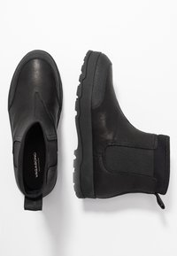 Černé kožené a elastické kotníkové boty se robustní podešví a poutkem pro snadné obutí. Hladký povrch, minimalistický design.