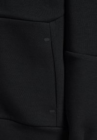 Svart sweatshirttyg med en slät textur. Har en sidoficka med en liten, rund hårdvarupunkt. Enkelt, minimalistiskt design.