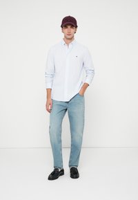 Ανοιχτό μπλε πουκάμισο με ρίγες, ανοιχτό χρώμα τζιν και μπορντό καπέλο. Μαύρα παπούτσια συμπληρώνουν την εμφάνιση, με καλή εφαρμογή.