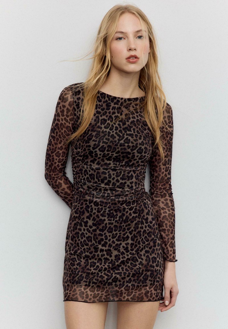 Robe longue à manches longues en tissu transparent, présentant un imprimé léopard marron et noir, une coupe ajustée et des côtés froncés. Texture lisse avec un col rond.