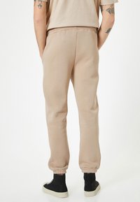 Beige sweatpants med elastiske manchetter og talje, lavet af blødt materiale, har en afslappet pasform og diskrete lommer. Sorte høje sneakers.