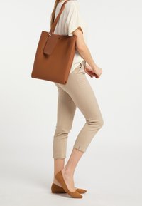 Borsa a tracolla marrone realizzata in materiale sintetico liscio, con forma rettangolare, lunga tracolla e un'etichetta staccabile.