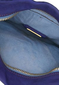 Interno di una borsa in suede viola con una fodera a strisce blu chiaro, dotata di una cerniera dorata e di un'etichetta in oro visibile.