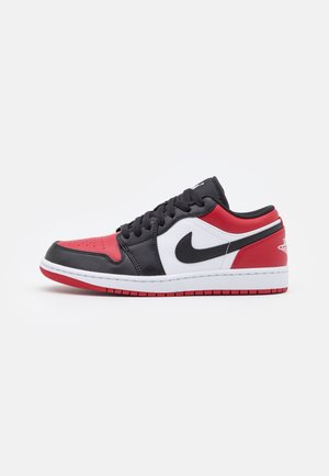 Lav sneaker med sorte, røde og hvide paneler, sorte snørebånd, Nike-logo og rød sål på hvid baggrund.