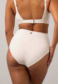 Krämfärgade högmidjade trosor i en texturerad ribbad tyg med en liten metallisk detalj på baksidan, med en slät yta och minimala sömmar.