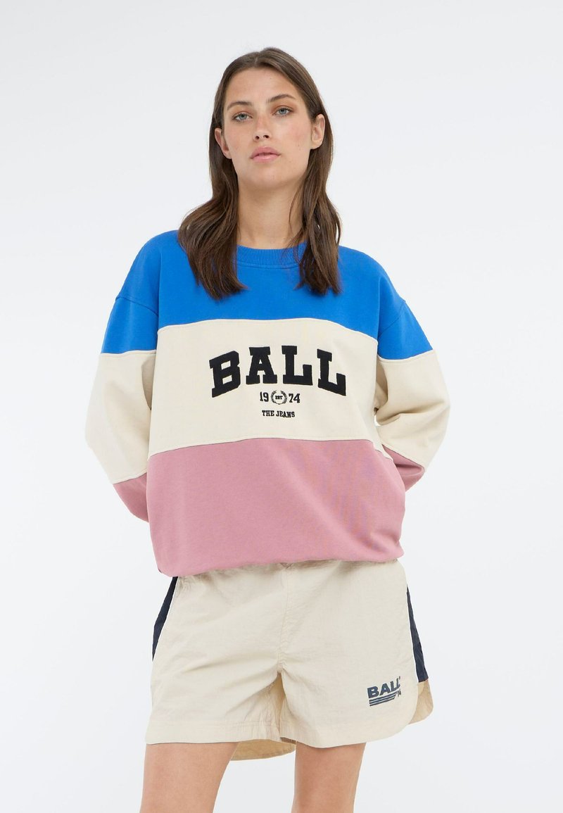Felpa color-block in blu, crema e rosa con grafica "BALL" e anno "1974". Abbinata a pantaloni beige con accenti laterali.