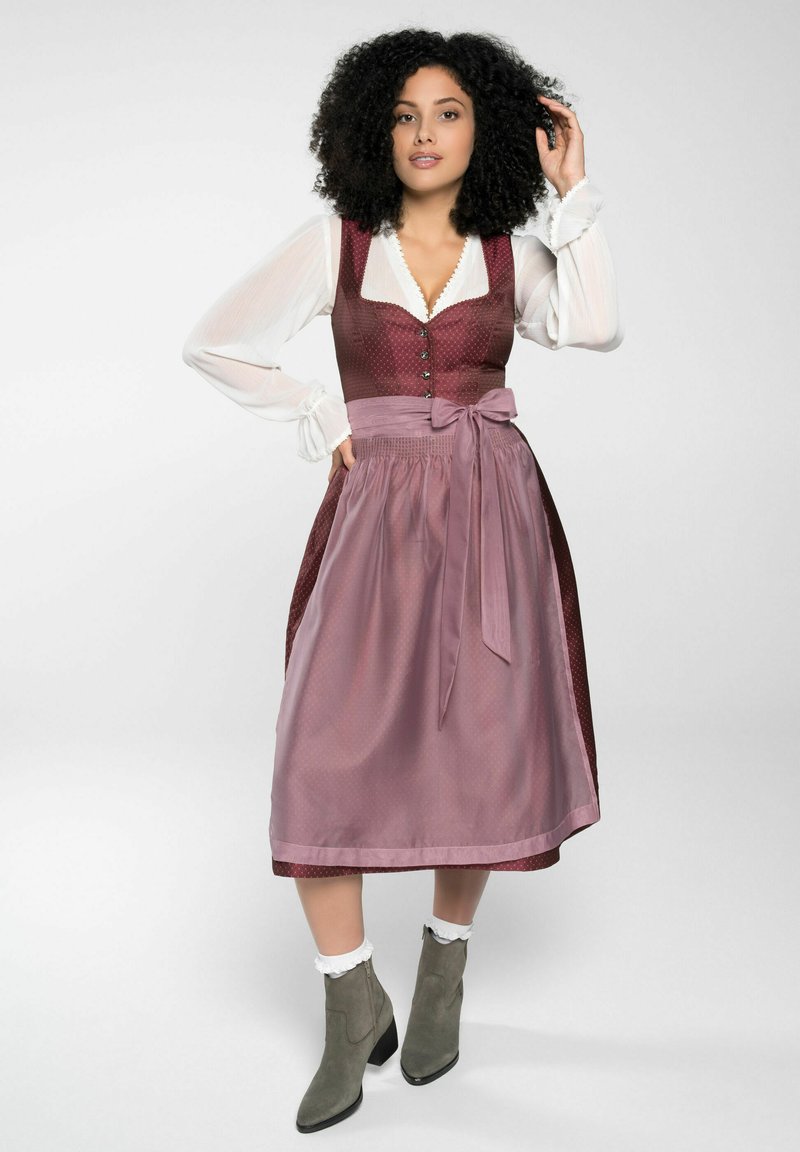 Robe traditionnelle avec un corsage bordeaux et un motif à pois, une jupe rose pâle, et un nœud. Complétée par des bottines grises à la cheville.