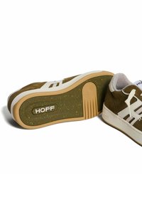 Sneaker in suede marrone con accenti bianchi, suola in gomma testurizzata color tan, e soletta green con macchie, caratterizzati da un logo distintivo sulla suola.