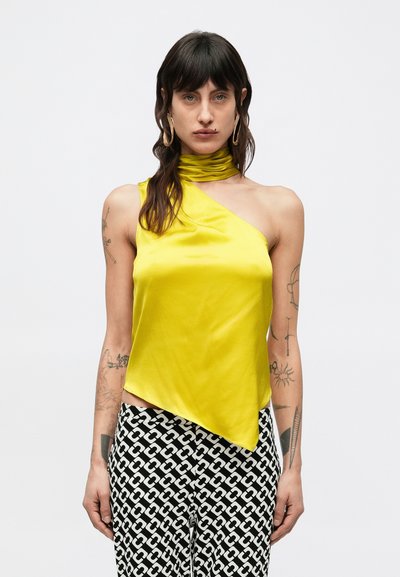 Haut asymétrique en satin jaune avec un col froncé. Porté avec un pantalon noir et blanc à motifs, orné d'un design à maillons de chaîne.