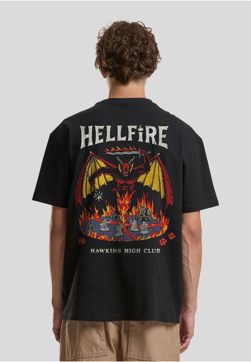 T-shirt en coton noir avec un grand graphique multicolore au dos représentant un diable, des flammes et le texte « HELLFIRE HAWKINS HIGH CLUB ».