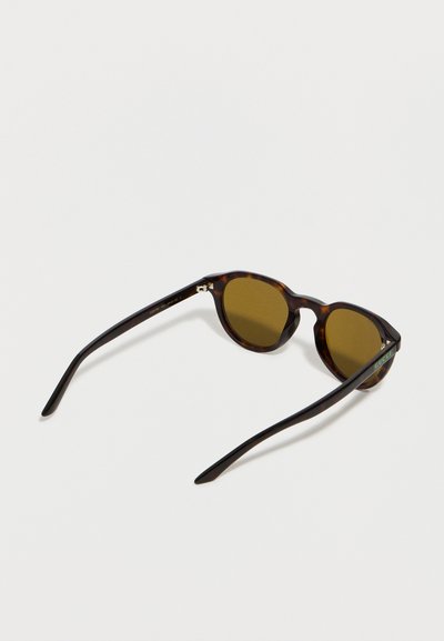 Lunettes de soleil rondes en écaille de tortue avec verres marron et branches fines, avec un petit logo de marque sur la branche droite.