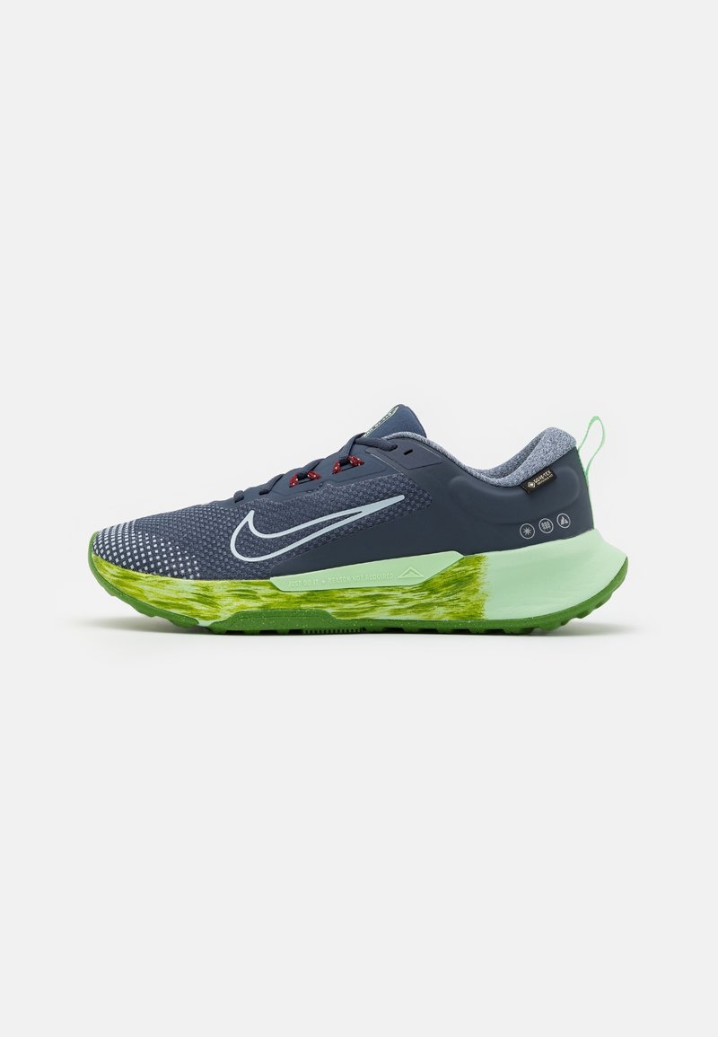 Chaussure de course Nike bleue et verte avec tige en mesh, lacets rouges, swoosh blanc et semelle verte texturée sur fond blanc.