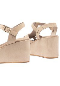 Sandali con zeppa in camoscio beige, design con fascette incrociate, fibbia regolabile, soletta testurizzata, tacco a zeppa curvato e finitura cromatica liscia.