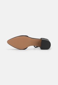Black high heel shoe with a pointed toe and a textured black outsole, featuring a tan sole and a block heel. Smooth upper material.
