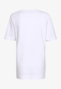 Bílý krátký rukáv T-shirt zobrazený zezadu na jednolitém světlém pozadí.