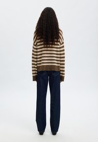 Brun och krämrandig tröja, stickad, med en lös passform. Matchad med mörkblå vida jeans. Enhetlig bakgrund.