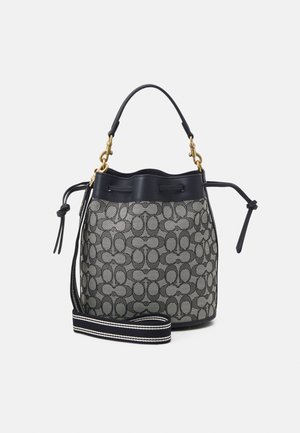 Schwarze und beige gemusterte Beuteltasche mit schwarzem Lederbesatz, goldfarbenen Metallteilen, Tragegriff oben und verstellbarem schwarz-weiß gestreiftem Schultergurt.