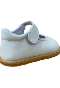 Zapato infantil de cuero blanco con punta redonda, parte trasera redondeada, corte lateral y correa de velcro ajustable. Suela de goma texturizada para mayor agarre.