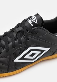 Čierne kožené futbalové topánky s bielymi akcentmi, so štruktúrovaným dizajnom, gumovou podrážkou a kontrastným logom na jazyku.
