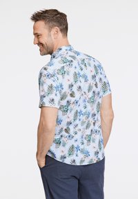 Maglietta a maniche corte in tessuto azzurro chiaro con stampa floreale tropicale che presenta foglie verdi e fiori blu, vestibilità aderente, orlo curvo.