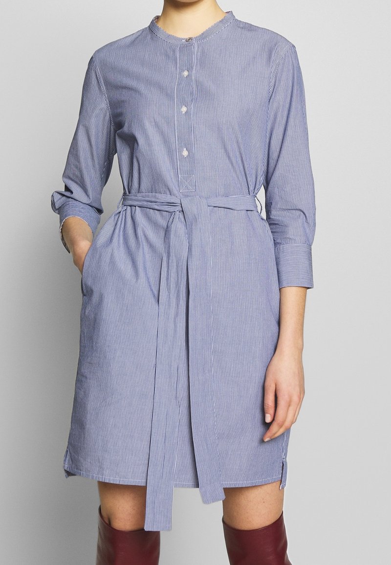 Modrá a bílá pruhovaná šatová košile s kulatým výstřihem, knoflíkovým zapínáním, dlouhými rukávy a vázaným pasem, vyrobená z lehkého materiálu.