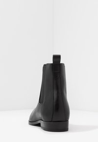 Bottine en cuir noir avec panneaux latéraux élastiques, bout arrondi et petit talon empilé. Dotée d'une languette à l'arrière pour un enfilage facilité.