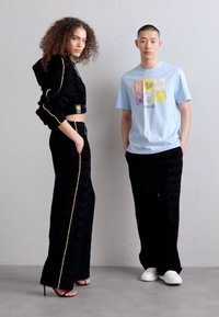 Ensemble coordonné noir texturé avec des accents dorés ; hoodie court et pantalon taille haute. Le modèle à gauche porte des sandales à talons ; à droite, un t-shirt graphique bleu clair.