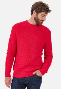Pull rouge en maille avec motif tissé texturé, col rond, poignets et ourlet côtelés. Porté avec un jean bleu.