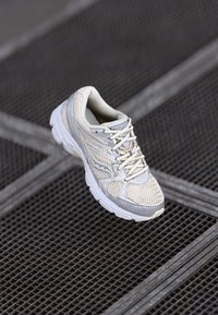 Baskets de course gris clair avec des panneaux en maille, languette rembourrée et lacets blancs. Présentent une semelle texturée et un marquage discret sur le côté.