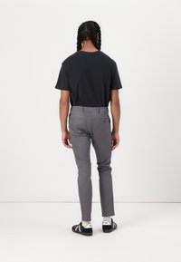 Camiseta negra de manga corta combinada con pantalones ajustados grises. Los pantalones tienen bolsillos traseros; la persona lleva zapatillas negras con detalles en blanco.