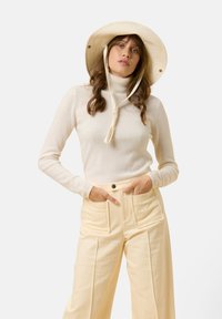 Krämfärgad rullkragsweater med långa ärmar, matchad med höga ljusgula byxor med vida ben och framträdande framfickor. Hatt med bred brätte.