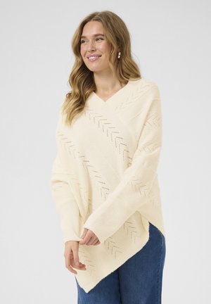 Strickponcho in sanftem Creme, mit diagonalen Fischgrätmustern und weitem Halsausschnitt. Betont mit gerippten Ärmeln und Saum.