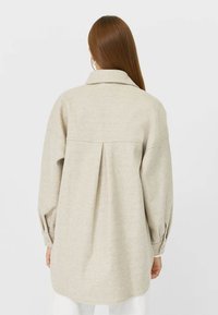 Beige wollen blend hemd met een plooi aan de achterkant, oversized pasvorm, puntige kraag en knoopmanchetten. Glad textuur, gebogen zoom.