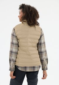 Beige isolerad väst med hög krage, quiltat mönster och en rutig skjorta som syns under, med ärmlängd. Slät textur, lätt konstruktion.